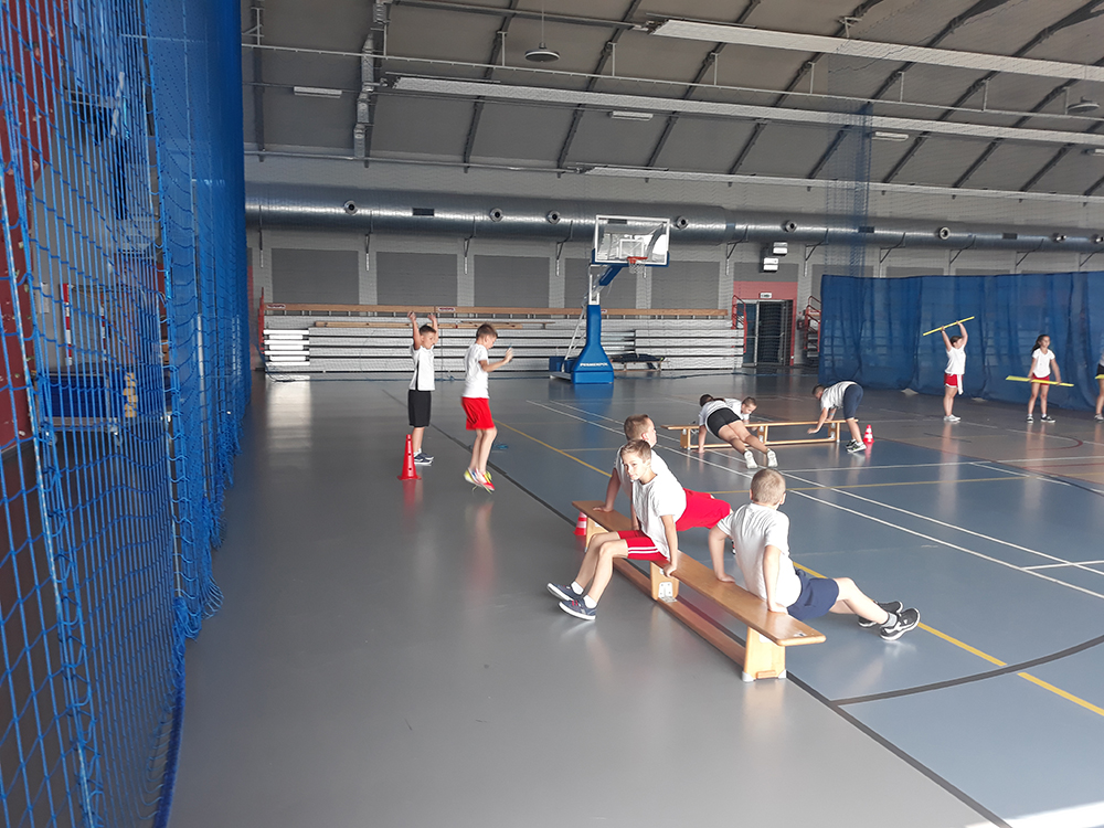 Uczniowie ćwiczący na hali sportowej w zalecanych odstępach.