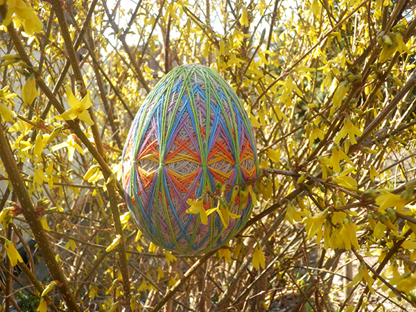Kolorowe jajo wielkanocne wykonane metodą haftu Temari na tle żółtych forsycji