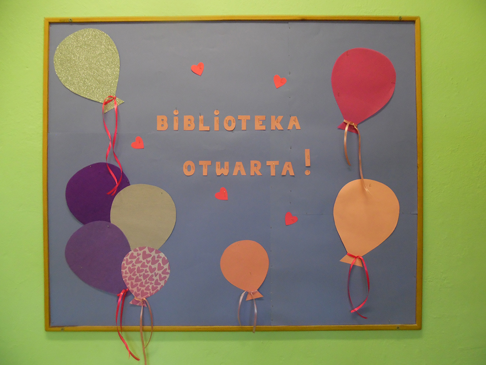 Główna tablica biblioteczna. Na fioletowym tle przypięto kolorowe papierowe balony. Pomiędzy nimi odczytamy napis - Biblioteka otwarta!