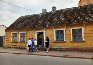 Przed drewnianym domem z detalami przypominającymi lwy przy ulicy Rawskiej