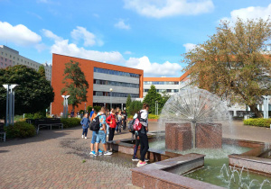 Przed nowoczesnym budynkiem Uniwersytetu Łódzkiego i fontanną w kształcie dmuchawca