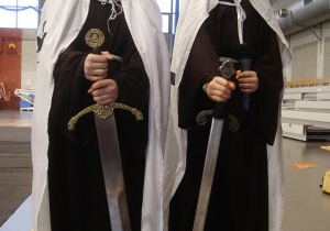 Uczniowie przebrani za krzyżaków przekazują dwa nagie miecze.