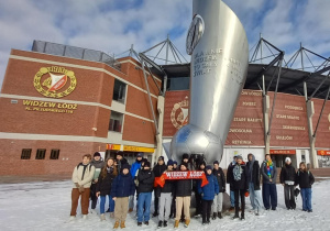 Uczestnicy wycieczki przed stadionem Widzewa przy pomniku w kształcie pochodni