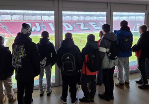 Uczestnicy wycieczki obserwują trening odbywajacy się na murawie stadionu z okien loży dla VIPów
