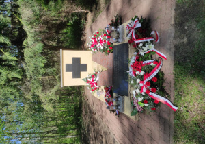 Pomnik pomordowanych w lesie w Babichach, upamiętniający polskich patriotów zamordowanych przez hitlerowców w 1945 roku. Na zdjęciu widać miejsce pamięci otoczone lasem, udekorowane kwiatami, biało-czerwonymi wstęgami oraz zapalonymi zniczami.