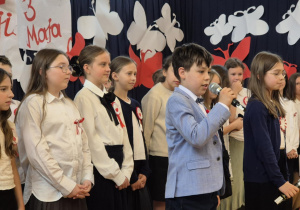 Uczeń recytujący wiersz, w tle pozostali występujący