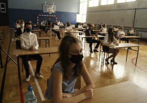 Uczniowie klas ósmych siedzący przy ławkach na sali gimnastycznej, oczekujący na rozpoczęcie egzaminu ósmoklasisty z języka polskiego.