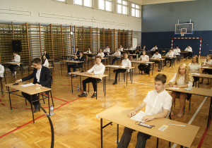Uczniowie klas ósmych siedzący przy ławkach na sali gimnastycznej tuż przed rozpoczęciem egzaminu bez maseczek ochronnych.
