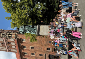 Uczniowie klasy stoją obok pomnika Mikołaja Kopernika.