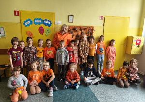 Uczniowie z klasy 1c wraz z wychowawcą, ubrani na pomarańczowo przed swoją salą.