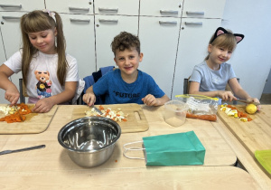 Anastazja, Wojtek i Marianka z uśmiechem kroją świeże warzywa.