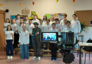 Uczniowie klasy 5a ustawieni w rzędach tworzących chór w czasie rejestrowania nagrania kamerą