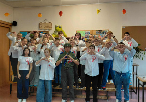 Uczniowie klasy 5a z nauczycielem języka polskiego pokazują serca ułożone z dłoni