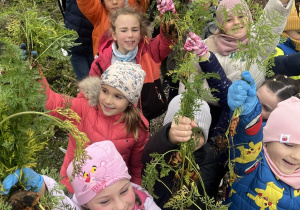 Dzieci z uśmiechem prezentują swoje kolorowe, świeże zbiory z ogródka.