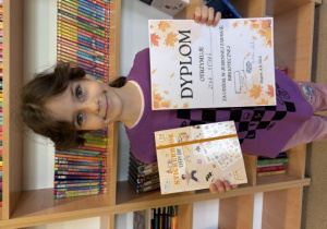 Uczennica klasy 2 A z dyplomem oraz nagrodą zdobytą w konkursie bibliotecznym.