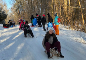 Uczestnicy zajęć zjeżdżają z górki na sankach