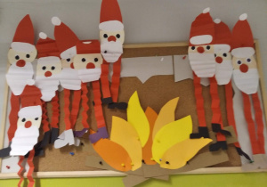 Mikołaje - ludziki przy ognisku wywieszone na tablicy korkowej. Prace wykonane pod opieką Pani A. Kosińskiej.