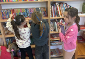 Uczennice klasy pierwsze przeglądają księgozbiór biblioteki szkolnej.