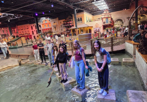 Dziewczynki i chłopcy pokonują wodną przeszkodę skacząc po kamieniach