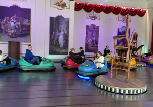 Opiekunowie i uczestniczki wycieczki jeżdżą samochodzikami elektrycznymi