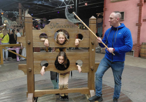 Dziewczynki zakute w średniowieczne dyby pilnowane przez opiekuna uzbrojonego w topór