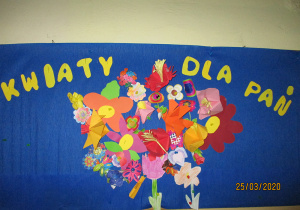 Dekoracja wiosenna związana z Dniem Kobiet. Kolorowe kwiaty wykonane z papieru, przyklejone na niebieskim tle. Na górze żółty napis „KWIATY DLA PAŃ”.