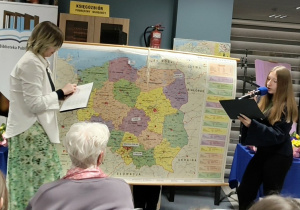 Uczennice klasy ósmej recytują wiersz na tle mapy Polski