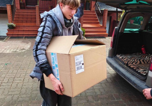 Przewodniczący Samorządu Uczniowskiego niesie pudło z paczkami z samochodu do siedziby Fundacji Krwinka.