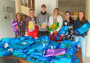 Wspólne zdjęcie pracowników Fundacji Krwinka oraz delegacji Samorządu Uczniowskiego z opiekunem. Na stole widnieją przygotowane paczki dla dzieci.