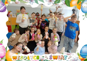 Zdjęcie ukazuje uczniów trzymających w rękach skarpetkowe zające. Pod zdjęciem widnieje napis: „Wesołych Świąt!”.