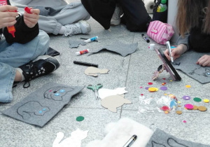 Dziewczynki ozdabiają szare szablony kolorowymi filcowymi elementami.