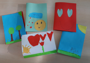 Zdjęcie przedstawiające kolorowe kartki wykonane dla chorego kolegi. Wśród prac widnieją słoneczka, serduszka, drzewa, kwiaty i uśmiechnięte buźki.