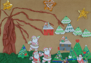 Tablica korkowa z dekoracją świąteczną. Na zdjęciu widać drzewo bez liści, złote gwiazdy, postać Mikołaja wycięta z papieru i choinki z kolorowego papieru i serwetek.
