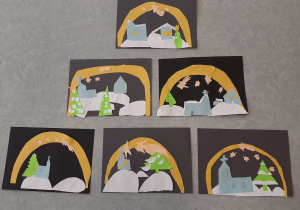 Prace uczniów przedstawiające Świętą nocą. Na czarnym kartonie przedstawiono żółte gwiazdy, kościół, śnieg, choinki i domy.