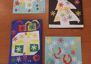 Zdjęcie przedstawiające kartki świąteczne. Na kartonach w kolorze czarnym, niebieskim i błękitnym przyklejone są choinki, prezenty i śnieżynki.
