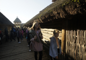 Grupa uczniów idąca między drewnianymi chatami.
