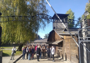 Uczniowie wraz z opiekunami i przewodnikiem zgromadzeni przed bramą główna Auschwitz.