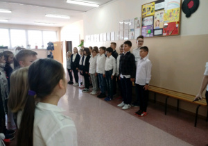 Uczniowie klas IV-VIII stoją na korytarzu i śpiewają hymn. Budynek B, 2 piętro.