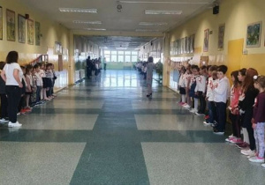 Uczniowie klas I-III stoją na korytarzu i śpiewają hymn. Budynek A, 2 piętro.