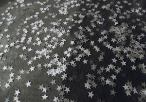 Zdjęcie przedstawia rozrzucone na dywanie srebrnoszare gwiazdki.