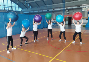 Uczennice klas ósmych ćwiczące z piłkami piłkami.