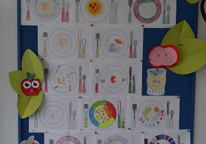 Tablica korkowa przedstawiająca prace uczniów związane ze zbilansowanym odżywianiem. Uczniowie projektowali własną zastawę stołową. Kolorowe wzory na talerzach oraz kolorowe sztućce. Na talerzach znajdują się różnorodne potrawy. Prace wykonane w gr. I.
