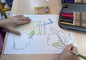 Uczniowie wykonują prace plastyczne - kolorują kredkami szkic jabłka.