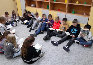 Uczniowie czytają książki siedząc w kole.