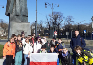 Uczestnicy wyprawy przed pomnikiem Marszałka Piłsudskiego w Łodzi, trzymają flagę państwową