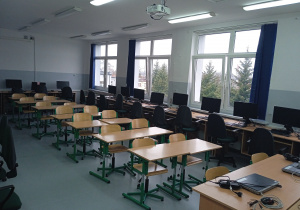 Zdjęcie przedstawia odnowioną pracownię komputerową z ustawionymi komuterami, ławkami i stolikami uczniowskimi